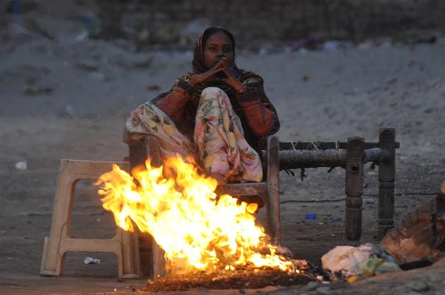 A woman warms herself from the cold beside a fire.
