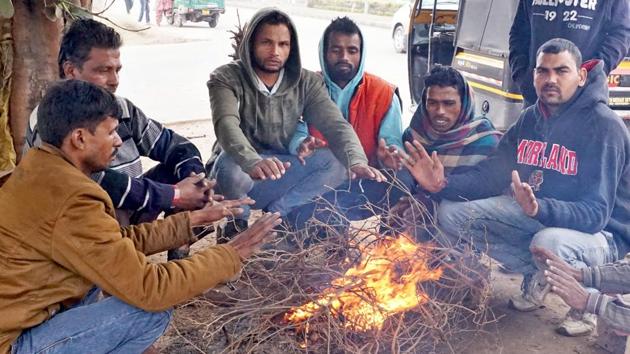Men sit around a bonfire to protect themselves from the cold at Airport Road in Mohali. (Sushil Prajapati/HT)