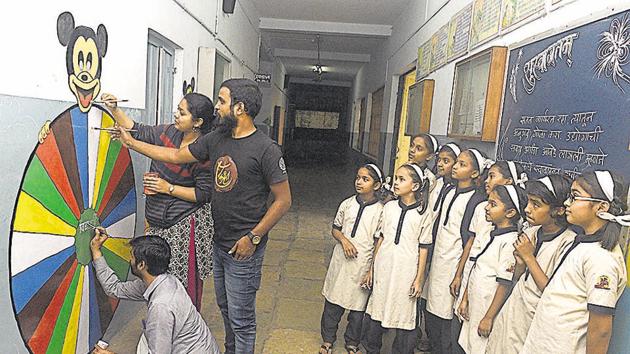 Ashish Patil (sitting), Sushma Kamble (standing) and Sachin Tonde give finishing touches to a graffiti as students of Vidya Niketan school watch them paint their school walls.(Pratham Gokhale/HT Photo)