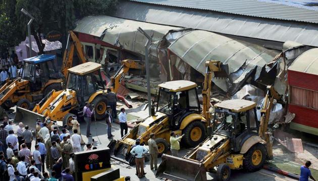 Onlookers gather around as BMC bulldozers take down illegally constructed eateries in the Kamala Mills compound following a fire incident in Mumbai. (PTI) Onlookers gather around as BMC bulldozers take down illegally constructed eateries in the Kamala Mills compound following a fire incident in Mumbai. (PTI)
