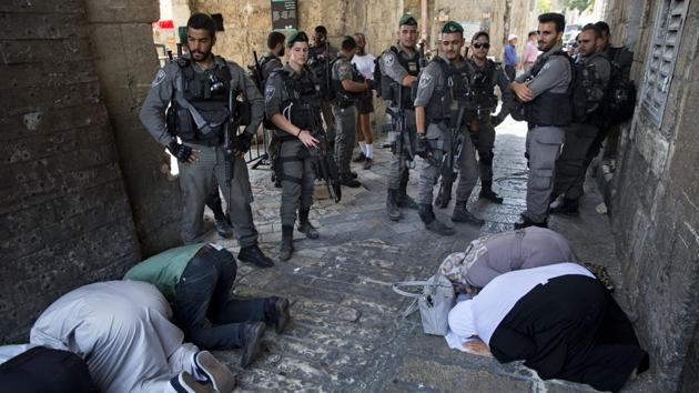 Palestinians pray as Israeli border police officers stand guard at the Lion’s Gate in the Old City. Dozens of Muslims on July 25, 2017 prayed in the street outside a major Jerusalem shrine, heeding a call by clerics not to enter the site until a dispute with Israel over security arrangements was settled. (Oded Balilty / AP) Palestinians pray as Israeli border police officers stand guard at the Lion’s Gate in the Old City. Dozens of Muslims on July 25, 2017 prayed in the street outside a major Jerusalem shrine, heeding a call by clerics not to enter the site until a dispute with Israel over security arrangements was settled. (Oded Balilty / AP)