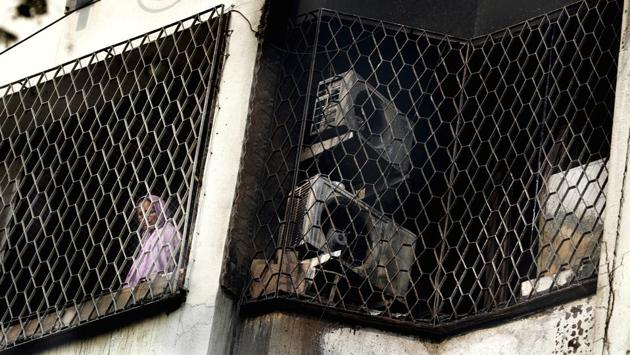 A woman looks out from the window of a residential building in Mumbai’s Andheri East after it was partially damaged in an early morning fire which claimed the lives of four people, including two children and left five injured. (Rafiq Maqbool / AP)