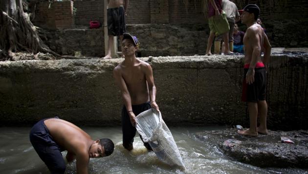 Douglas (C) holds a sack in the Guaire as he and others pull mud up from the riverbed to sift for treasure. The river and its scavengers go largely unnoticed by Caracas residents speeding by on the city’s main highway, blocked from view by concrete barriers. (Ariana Cubillos / AP) Douglas (C) holds a sack in the Guaire as he and others pull mud up from the riverbed to sift for treasure. The river and its scavengers go largely unnoticed by Caracas residents speeding by on the city’s main highway, blocked from view by concrete barriers. (Ariana Cubillos / AP)