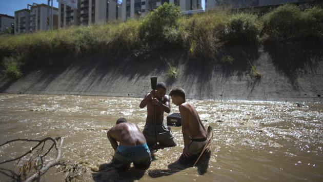 Angel Villanueva (C) breaks up mud at the bottom of Guaire in Caracas. He says people don’t want to touch him, or come near because the toxic odour from Guaire’s waters, reminiscent of fuel lingers on his body. They fear an infection from his being in the river, but despite jibes he remains hooked. (Ariana Cubillos / AP) Angel Villanueva (C) breaks up mud at the bottom of Guaire in Caracas. He says people don’t want to touch him, or come near because the toxic odour from Guaire’s waters, reminiscent of fuel lingers on his body. They fear an infection from his being in the river, but despite jibes he remains hooked. (Ariana Cubillos / AP)