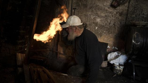 Goumas looks into the fire as he tries to control the temperature of the furnace in his workshop. “Then I’ll never have to leave this place,” he said, provided he can raise the necessary funds. (Petros Giannakouris / AP)