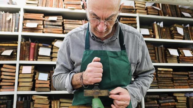 Brian Cole a bookbinder responsible for the maintenance of the books embosses the spine of a book with gold foil in his workshop at the library. (Ian Forsyth / Getty Images)