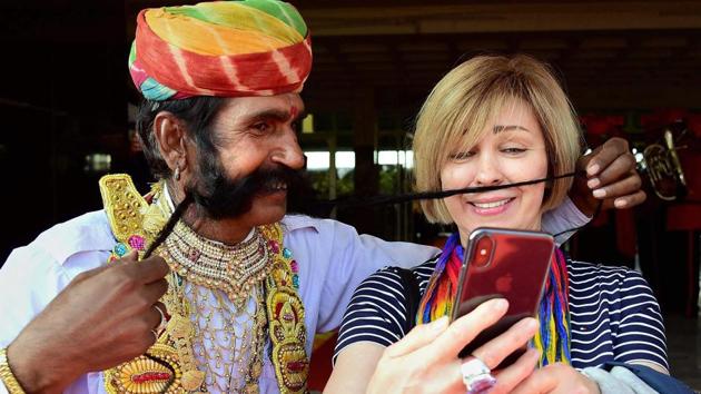 A foreign tourist clicks a selfie with a Rajasthani artiste with long moustache in Rajasthan’s Bikaner.(PTI FILE PHOTO)