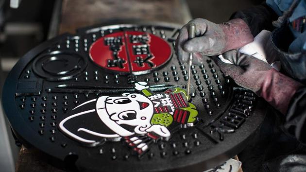 Japanese employee Isamu Kamiya paints a manhole cover. Cover designs must have the same friction level no matter which direction humans or cars come from to avoid slippage. This need for friction resulted in placing extra streaks of clouds, sea waves or tiny stars in the background, giving birth to “condensed designs”. (Behrouz Mehri / AFP) Japanese employee Isamu Kamiya paints a manhole cover. Cover designs must have the same friction level no matter which direction humans or cars come from to avoid slippage. This need for friction resulted in placing extra streaks of clouds, sea waves or tiny stars in the background, giving birth to “condensed designs”. (Behrouz Mehri / AFP)