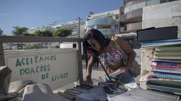 A woman peruses books next to a sign reading “We accept donations of books” at a stand set by Marcio who came to Rio seeking a fortune, but could only afford to live on the street. All that changed when a friend taught him how to build a sandcastle. “I learned a lot from reading and I think my castle is a mixture of styles, between Niemeyer and Gaudi,” he said of his palace. (Mauro Pimentel / AFP) A woman peruses books next to a sign reading “We accept donations of books” at a stand set by Marcio who came to Rio seeking a fortune, but could only afford to live on the street. All that changed when a friend taught him how to build a sandcastle. “I learned a lot from reading and I think my castle is a mixture of styles, between Niemeyer and Gaudi,” he said of his palace. (Mauro Pimentel / AFP)