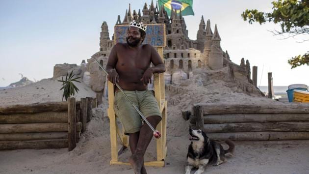 With a crown on his head, Marcio sits on a throne in front of his sand castle with his dog Humana. Meanwhile, he doesn’t seem to tire of endlessly carving his fragile palace with a knife or a shovel. Like his hero Gaudi’s Sagrada Familia cathedral in Barcelona, the largest unfinished basilica in the world, Marcio’s creation is a perpetual work in progress. (Mauro Pimentel / AFP) With a crown on his head, Marcio sits on a throne in front of his sand castle with his dog Humana. Meanwhile, he doesn’t seem to tire of endlessly carving his fragile palace with a knife or a shovel. Like his hero Gaudi’s Sagrada Familia cathedral in Barcelona, the largest unfinished basilica in the world, Marcio’s creation is a perpetual work in progress. (Mauro Pimentel / AFP)