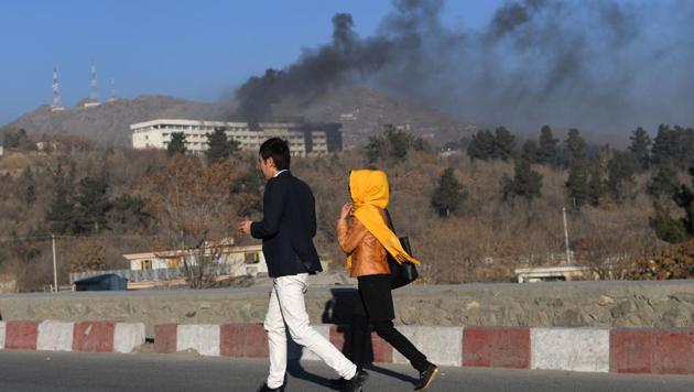 Afghans walk near the Intercontinental Hotel as smoke billows during a fight between gunmen and Afghan security forces in Kabul.(AFP Photo)