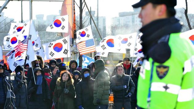 People hold US and South Korean flags (in background) as they protest against the unified Korea female ice hockey team at the Winter Olympics.(AFP)