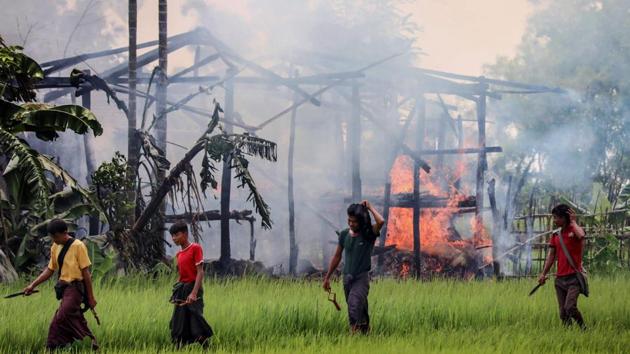 Unidentified men carry knives and slingshots as they walk past a burning house in Gawdu Tharya village near Maungdaw in Rakhine state of northern Myanmar.(AFP File Photo)