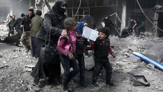 A Syrian woman and children run for cover amid the rubble of buildings following government bombing in Damascus. Eastern Ghouta, which houses around 400,000 residents, has remained under a crippling regime siege for the last five years. (Abdulmonam Eassa / AFP)