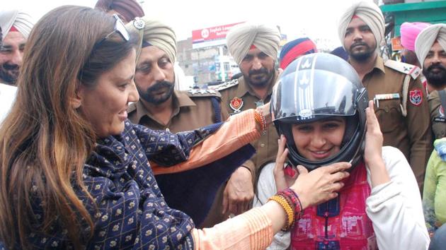 Veenu Badal, wife of local MLA and finance minister Manpreet Singh Badal, helping a woman wear a helmet at the launch of a traffic safety programme by the police in Bathinda on Friday.(Sanjeev Kumar/HT)