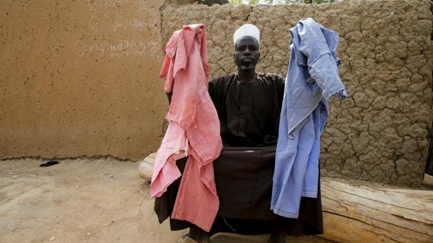 Alhaji Audu Danga, 50, sat outside his mud house clad in a dark kaftan holding up two dresses, one pink and one blue, used to distinguish school attire and home clothing for the students. His missing 20-year-old daughter Falmata Audu is among the oldest of the school’s 906 students. Most are between 11 and 19. (Afolabi Sotunde / REUTERS) Alhaji Audu Danga, 50, sat outside his mud house clad in a dark kaftan holding up two dresses, one pink and one blue, used to distinguish school attire and home clothing for the students. His missing 20-year-old daughter Falmata Audu is among the oldest of the school’s 906 students. Most are between 11 and 19. (Afolabi Sotunde / REUTERS)