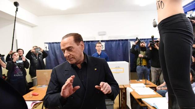 A Femen activist jumps on a table in front of Silvio Berlusconi, leader of right-wing party Forza Italia, to protest with bodypaint reading “Berlusconi, you have expired” at a polling station in Milan. (Miguel Medina / AFP) A Femen activist jumps on a table in front of Silvio Berlusconi, leader of right-wing party Forza Italia, to protest with bodypaint reading “Berlusconi, you have expired” at a polling station in Milan. (Miguel Medina / AFP)