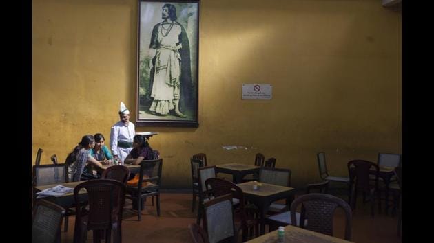 A waiter serves schoolgirls beneath a portrait of Rabindranath Tagore in the Indian Coffee House, Kolkata, 2013. Freedman’s photographs employ longing and escape meticulously, especially in their depiction of empty chairs and tables, portraits of people staring into nothing while sipping on their coffee. (© Stuart Freedman / Tasveer)