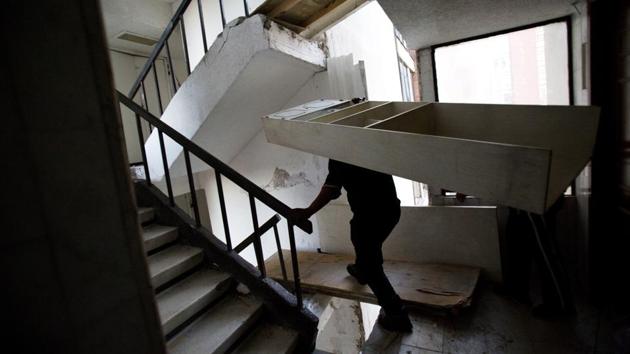 A man carries a bookshelf down a staircase with gaps that have been covered with boards. Displaced residents received 3,000 pesos ($160) each month for the first three months from the government. The idea was that they would rent apartments elsewhere. But residents say that wasn’t enough and they fear looters will clear out their possessions if they leave. (Rebecca Blackwell / AP)