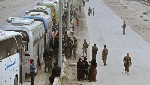 Syrian regime forces stand near buses waiting at the entrance of Harasta in Eastern Ghouta, on the outskirts of Damascus, on March 22, 2018, after a deal was struck with the rebels in the area to evacuate the town. (AFP) Syrian regime forces stand near buses waiting at the entrance of Harasta in Eastern Ghouta, on the outskirts of Damascus, on March 22, 2018, after a deal was struck with the rebels in the area to evacuate the town. (AFP)
