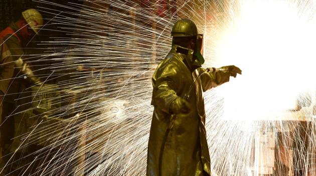 An employee works in front of the blast furnace past rolls of sheet steel at a mill of German steel producer Salzgitter AG. Steel making has existed for millennia, but not on such a massive scale until 19th century. It is a crucible process of producing steel from iron ore and scrap where impurities are removed from raw iron and other elements are added to produce different grades of steel.  (Alexander Koerner / Getty Images) 