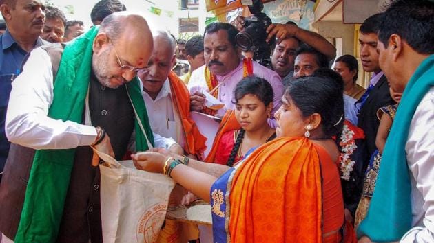 BJP president Amit Shah collects food grains from a farmer’s family during a statewide door-to-door campaign ahead of Karnataka assembly elections at Doddabathi village in Davanagere on Tuesday.(PTI Photo)