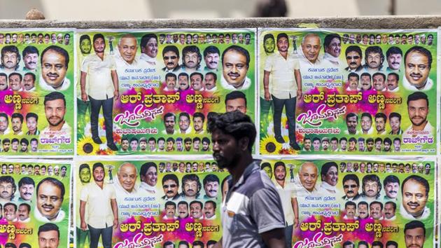 A pedestrian walks past election campaign posters for Karnataka elections 2018 in Bengaluru.(Bloomberg File Photo)