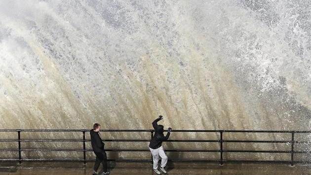 Young men stand by as a giant wave crashes, near Cullercoats on the North East Coast of England, as the weather takes a cold turn over the Easter weekend. (Owen Humphreys / PA via AP)