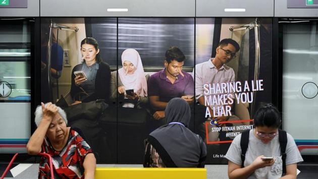 Commuters sit in front of an advertisement discouraging the dissemination of fake news, at a train station in Kuala Lumpur, Malaysia, on March 28.(Reuters File Photo)