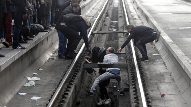 Passengers assist a woman who fell off a platform trying to cross railroad tracks at Gare de Lyon train station as unions staged a mass strike in Paris, France. (Francois Mori / AP)