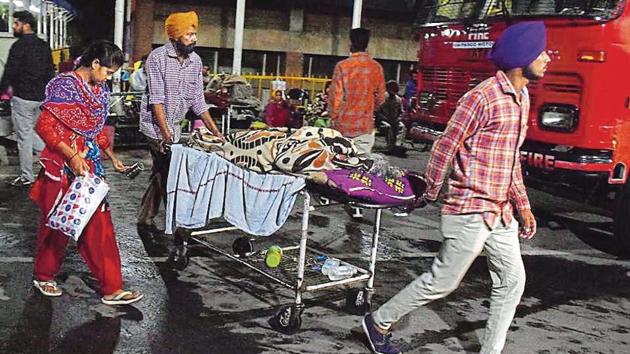 A patient being evacuated from the Emergency block after a fire in an operation theatre; (right) firemen breaking windowpanes to let out smoke at the PGIMER in Chandigarh on Wednesday.(Sikander Singh/HT)