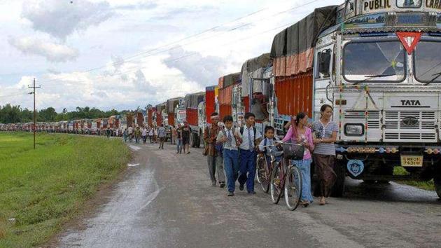 Schoolchildren and others walk past empty trucks parked in a row, waiting to be escorted by police to Assam to ferry supplies to Manipur, on the outskirts of Imphal.(PTI File Photo)