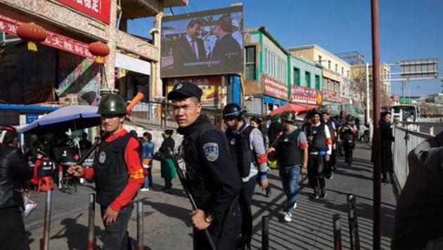 Armed civilians patrol the area outside the Hotan Bazaar where a screen shows Chinese President Xi Jinping in Hotan in western China's Xinjiang region.(AP File Photo)