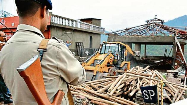 A JCB machine demolishes a part of an unauthorised hotel building as a policeman stands guard in Kasauli on Wednesday. (Sant Arora/ HT) A JCB machine demolishes a part of an unauthorised hotel building as a policeman stands guard in Kasauli on Wednesday. (Sant Arora/ HT)