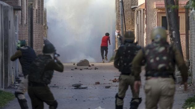 A protester runs for cover amid tear gas smoke as a policemen (left) fires pellet guns during a protest in Srinagar.(AP Photo)