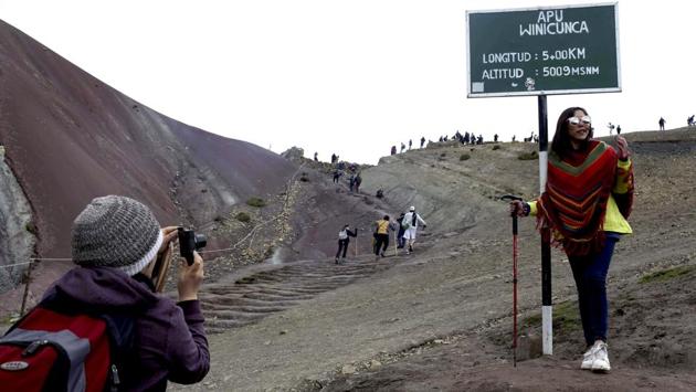 A tourist poses for a photograph at the entrance that leads to Rainbow Mountain. Visitors must climb for two hours to reach the peak in the Peruvian Andes which stands 16,404 feet above sea level. This tiresome trek turns worthy when the magical beauty of Rainbow Mountain unfurls before the eyes. (Martin Mejia / AP) A tourist poses for a photograph at the entrance that leads to Rainbow Mountain. Visitors must climb for two hours to reach the peak in the Peruvian Andes which stands 16,404 feet above sea level. This tiresome trek turns worthy when the magical beauty of Rainbow Mountain unfurls before the eyes. (Martin Mejia / AP)