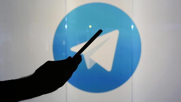 A man is seen as a silhouette as he checks a mobile device whilst standing against an illuminated wall bearing Telegram's logo in this arranged photograph in London.(Bloomberg)