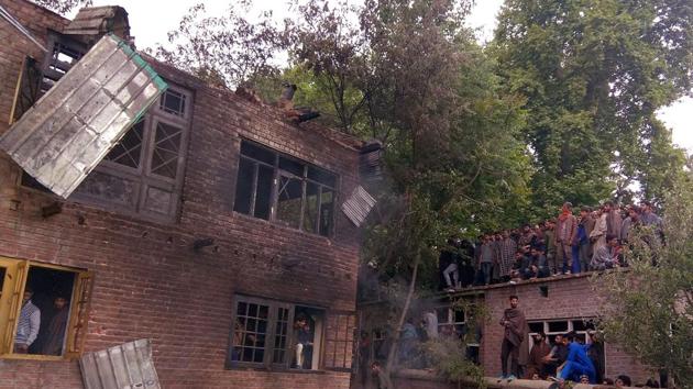 People look on at the damaged house where militant commanders were hiding during an encounter in Shopian. The civilian death toll in Sunday’s clashes between protestors and security forces in Shopian district of Jammu and Kashmir climbed to six after Iqbal Bhat, a youth who sustained a bullet injury in the abdomen, succumbed at SHMS Hospital in Srinagar this morning, a police official said. (PTI File)