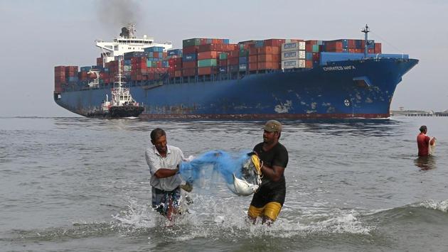 Fishermen carry bluefin trevally fish locally known as Vatta, as a cargo ship carrying containers moves in the Arabian Sea in Kochi on May 09, 2018. (Sivaram V / REUTERS) Fishermen carry bluefin trevally fish locally known as Vatta, as a cargo ship carrying containers moves in the Arabian Sea in Kochi on May 09, 2018. (Sivaram V / REUTERS)