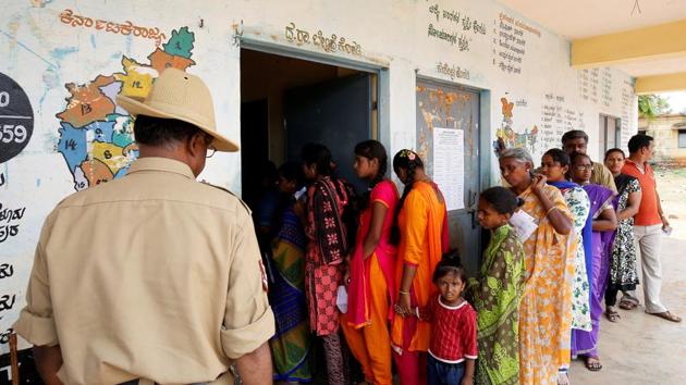 A policeman stands guard as people wait in a queue to cast their votes outside a polling station during Karnataka assembly elections at a village on the outskirts of Bengaluru.(Reuters Photo) A policeman stands guard as people wait in a queue to cast their votes outside a polling station during Karnataka assembly elections at a village on the outskirts of Bengaluru.(Reuters Photo)