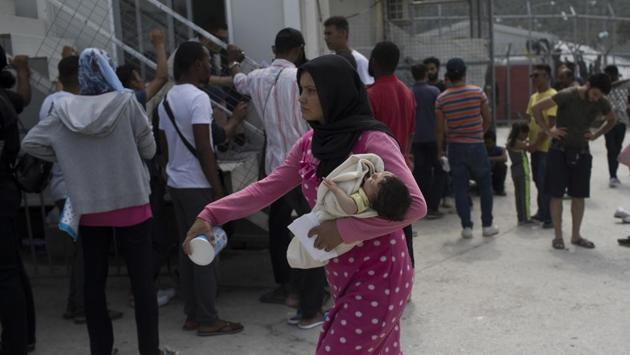 A woman walks with her baby as migrants and refugees wait outside UNHCR offices in Moria. Lesbos is facing a fourth summer of crisis. It’s one of five Greek islands near the coast of Turkey being used by the European Union to form a barrier to migration after more than a million people came through here in 2015-16. (Petros Giannakouris / AP) 
