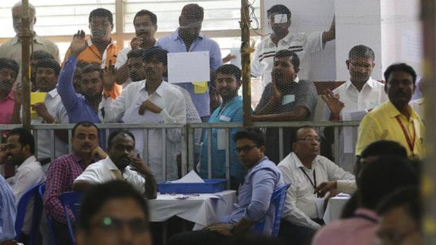 Election officials, in foreground, and agents of different political parties, wait for the counting of votes at a center in Bangalore. Where exit polls projected a hung assembly, the BJP was ahead in 104 seats, the Congress in 78 and the JD(S) 37 as of 4pm. Others/independents were ahead in three seats. (Aijaz Rahi / AP)