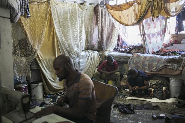 Malawian migrant shoe makers work inside their bedroom inside an abandoned building they occupy in downtown Johannesburg. Squatters say they want to see redevelopment that would give them a proper home, not force them to leave. (Bram Janssen / AP) Malawian migrant shoe makers work inside their bedroom inside an abandoned building they occupy in downtown Johannesburg. Squatters say they want to see redevelopment that would give them a proper home, not force them to leave. (Bram Janssen / AP)