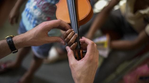 Pajak helps Riya build pressure on a violin’s strings. The project sponsors the cost of the violins for the children, their tuitions and also aims to facilitate higher education in music if the children wish to pursue the path. (Burhaan Kinu / HT Photo)
