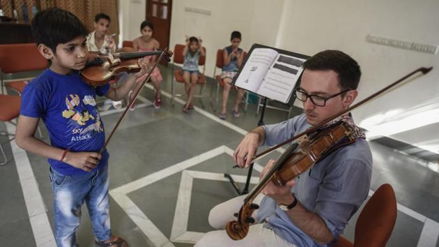 Ankush (L) and other students observe as their teacher Tomasz Pajak demonstrates on the violin. A teacher with the Delhi School of Music, Pajak is a Polish violinist and has been conducting weekly group and individual lessons with this group of children. (Burhaan Kinu / HT Photo)