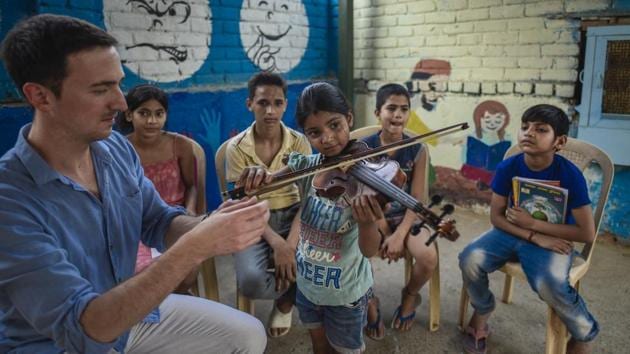 Riya, a Class 2 student plays the violin while other students and their instructor look on during music lessons for underprivileged children at Sanjay Camp in New Delhi. The project is being run by the Neemrana Music Foundation in collaboration with the Light Up, an NGO that works on emotional intelligence in the area. (Burhaan Kinu / HT Photo)