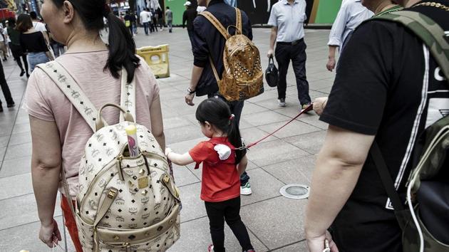 Pedestrians and a child wearing a child harness walks along a pedestrian shopping area in Shanghai, China.(Bloomberg)