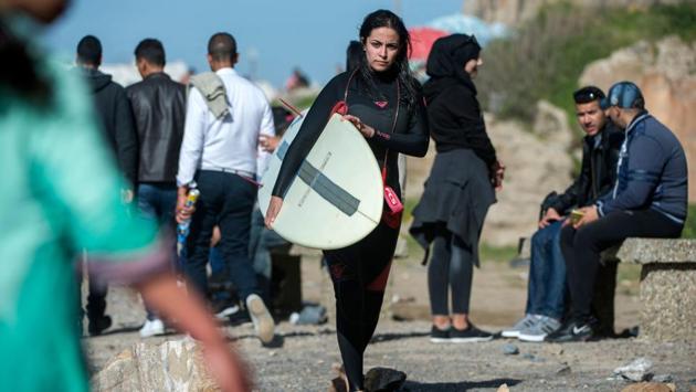 Meriem walks along the coastline after a session. In Mehdia, surf instructor Mounir believes there is no problem for girls surfing, but mentalities differ from beach to beach. Despite efforts to improve the status of women in Morocco, attitudes have been slow to change. A 2017 UN study found nearly 72% of men and 78% of women thinking “women who dress provocatively deserve to be harassed”. (Fadel Senna / AFP) Meriem walks along the coastline after a session. In Mehdia, surf instructor Mounir believes there is no problem for girls surfing, but mentalities differ from beach to beach. Despite efforts to improve the status of women in Morocco, attitudes have been slow to change. A 2017 UN study found nearly 72% of men and 78% of women thinking “women who dress provocatively deserve to be harassed”. (Fadel Senna / AFP)