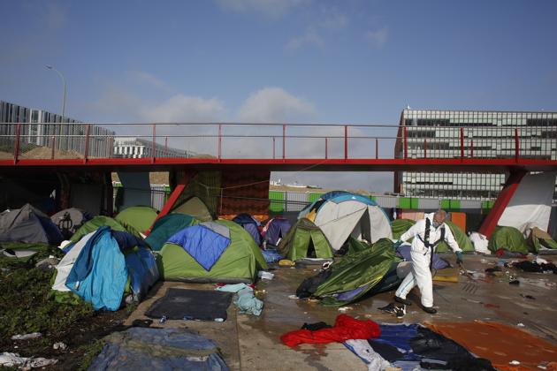 A Parisian town hall worker clears tents from the migrant makeshift camp. The camps have been at the heart of a political debate between French Interior Minister Gerard Collomb and Paris Mayor Anne Hidalgo over how to handle migrants. The mayor and dozens of associations pressed for the migrants to be sheltered once dislodged, as in the past. The minister dragged his feet. (Thibault Camus / AP) A Parisian town hall worker clears tents from the migrant makeshift camp. The camps have been at the heart of a political debate between French Interior Minister Gerard Collomb and Paris Mayor Anne Hidalgo over how to handle migrants. The mayor and dozens of associations pressed for the migrants to be sheltered once dislodged, as in the past. The minister dragged his feet. (Thibault Camus / AP)
