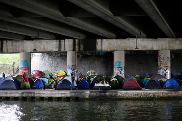 A migrant walks by tents in a makeshift camp along the Canal Saint Denis, in Paris. Police have cleared out some 28,000 migrants from Paris camps in the past three years, but the arrivals continue. (Thibault Camus / AP) A migrant walks by tents in a makeshift camp along the Canal Saint Denis, in Paris. Police have cleared out some 28,000 migrants from Paris camps in the past three years, but the arrivals continue. (Thibault Camus / AP)